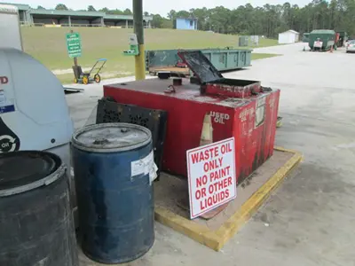 Picture of barrels and a red oil waste containment unit with a sign propped up against it saying waste oil only no paint or other liquid